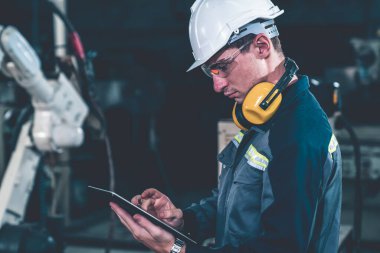 Bir atölyede usta bir robot kolla çalışan genç bir fabrika işçisi. Otomatik üretim teknolojisi için endüstriyel robot programlama yazılımı .