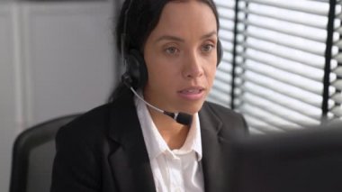 Competent african american female operator working on computer and while talking with clients. Concept relevant to both call centers and customer service offices.