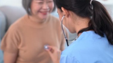 A contented retired senior woman being exterminated by her caregiver with a stethoscope at home. Medical care service, senior care at home.