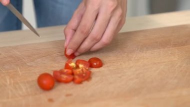 Close up hands holding a knife preparing a contented meal. Sliced tomatoes and other vegetables on the glass dish.