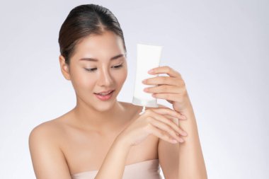 Gorgeous woman smiling holding mockup product for advertising text place, light grey background. Concept of healthcare for skin, beauty care product for advertising.