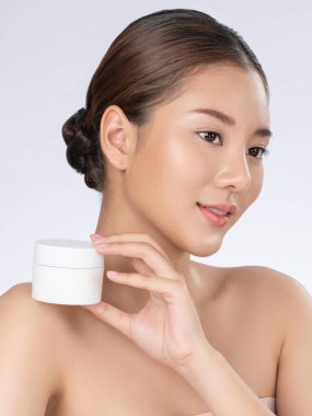 Gorgeous woman smiling holding mockup product for advertising text place, light grey background. Concept of healthcare for skin, beauty care product for advertising.