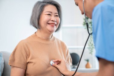 A contented retired senior woman being exterminated by her caregiver with a stethoscope at home. Medical care service, senior care at home.