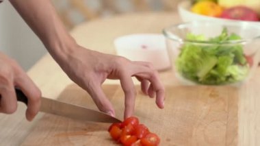 Close up hands holding a knife preparing a contented meal. Sliced tomatoes and other vegetables on the glass dish.