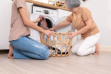 Daughter and mother working together to complete their household chores near the washing machine in a happy and contented manner. Mother and daughter doing the usual tasks in the house.