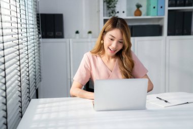 A young Asian female employee sitting at her desk in her office, sitting at desktop in workstation.