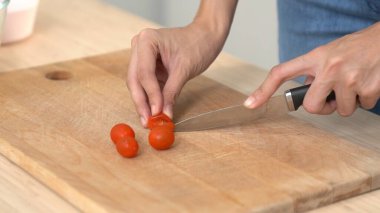 Close up hands holding a knife preparing a contented meal. Sliced tomatoes and other vegetables on the glass dish.