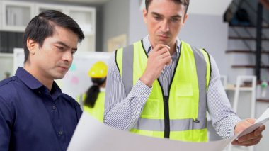 Competent investor investor discuss and brainstorm with engineers on blueprints or construction plans before putting them into action. Professional establishing investment for engineering projects.