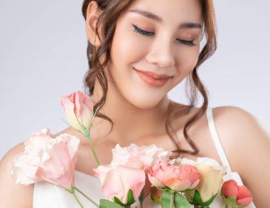 Closeup gorgeous female model with flawless fair skin and perfect makeup holding flowers bouquet. Woman receive flowers, white background.