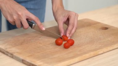 Close up hands holding a knife preparing a contented meal. Sliced tomatoes and other vegetables on the glass dish.