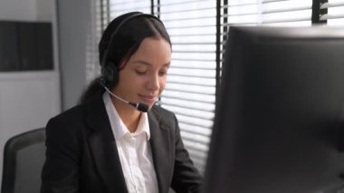 Competent african american female operator working on computer and while talking with clients. Concept relevant to both call centers and customer service offices.