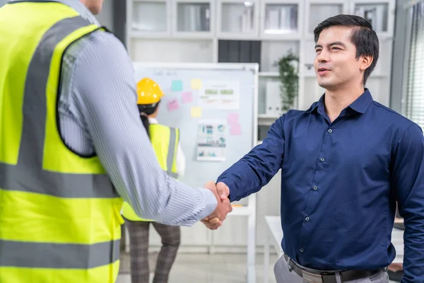 An engineer with a protective vest handshake with an investor in his office. Following a successful meeting, employee and employer form a partnership.