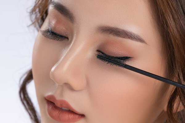 Closeup gorgeous young woman putting black mascara on her long eyelashes with brush. Beauty cosmetic concept. Female model with perfect skin.