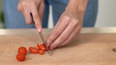 Close up hands holding a knife preparing a contented meal. Sliced tomatoes and other vegetables on the glass dish.