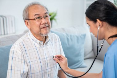 Caring young female doctor examining her contented senior patient with stethoscope in living room. Medical service for elderly, elderly sickness, declining health.