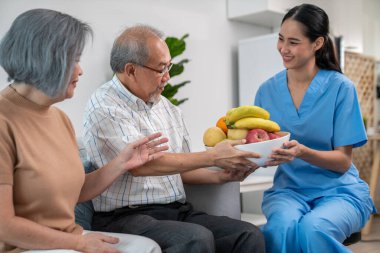 Contented senior couple taking a bowl of fruit from a nurse at home. Senior care at home.