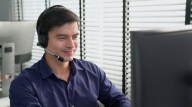 Young competent asian male call center agent working at his computer while simultaneously speaking with customers. Concept of an operator, customer service agent working in the office with headset.