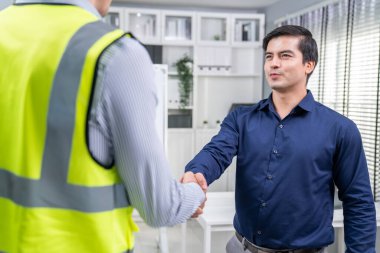 An engineer with a protective vest handshake with an investor in his office. Following a successful meeting, employee and employer form a partnership.