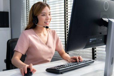 Competent female operator working on computer and while talking with clients. Concept relevant to both call centers and customer service offices.
