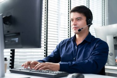 Young competent asian male call center agent working at his computer while simultaneously speaking with customers. Concept of an operator, customer service agent working in the office with headset.