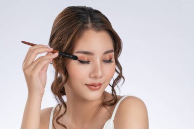 Gorgeous young woman putting black mascara on her long eyelashes with brush. Beauty cosmetic concept. Female model with perfect skin.