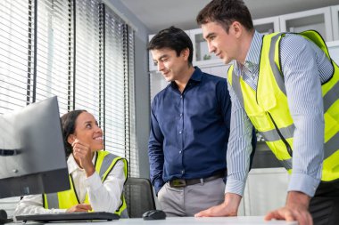 Happy multiracial team of competent engineers and investor smiles and works together at the table, cheerful and smart people brainstorming or meeting on engineering projects.