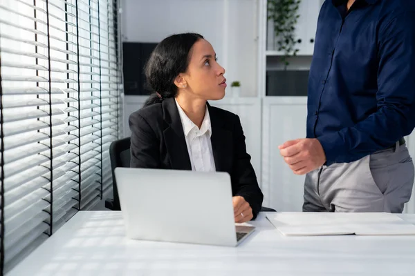 Competent female employee discussing with her colleague, employer using laptop at her office. Interpersonal relations among coworkers.