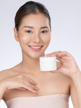 Gorgeous woman smiling holding mockup product for advertising text place, light grey background. Concept of healthcare for skin, beauty care product for advertising.