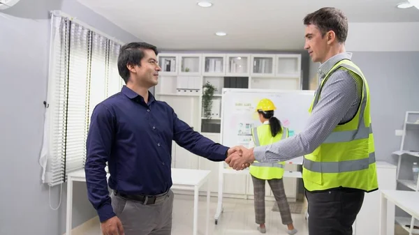 An engineer with a protective vest handshake with an investor in his office. Following a successful meeting, employee and employer form a partnership.