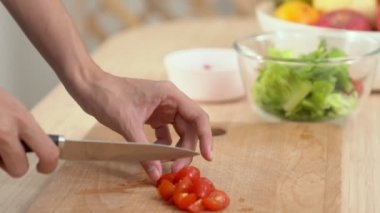 Close up hands holding a knife preparing a contented meal. Sliced tomatoes and other vegetables on the glass dish.