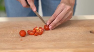 Close up hands holding a knife preparing a contented meal. Sliced tomatoes and other vegetables on the glass dish.