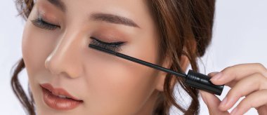 Closeup gorgeous young woman putting black mascara on her long eyelashes with brush. Beauty cosmetic concept. Female model with perfect skin.