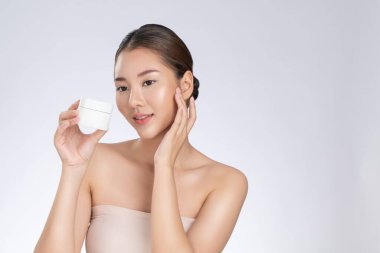 Gorgeous woman smiling holding mockup product for advertising text place, light grey background. Concept of healthcare for skin, beauty care product for advertising.