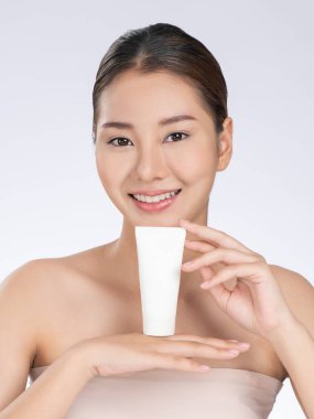 Gorgeous woman smiling holding mockup product for advertising text place, light grey background. Concept of healthcare for skin, beauty care product for advertising.