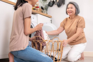 Daughter and mother working together to complete their household chores near the washing machine in a happy and contented manner. Mother and daughter doing the usual tasks in the house.