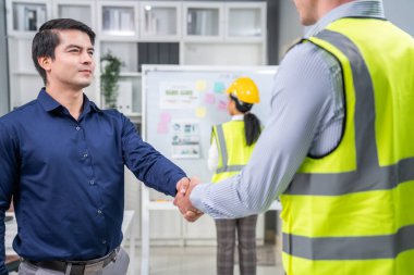 An engineer with a protective vest handshake with an investor in his office. Following a successful meeting, employee and employer form a partnership.