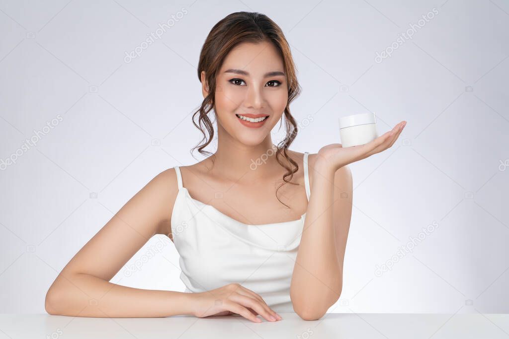 Gorgeous woman with makeup smiling holding mockup product for advertising text place, light grey background. Advertising concept for skin healthcare and beauty care products.