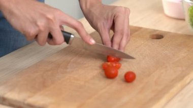 Close up hands holding a knife preparing a contented meal. Sliced tomatoes and other vegetables on the glass dish.