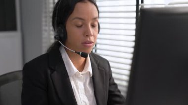 Competent african american female operator working on computer and while talking with clients. Concept relevant to both call centers and customer service offices.