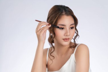 Gorgeous young woman putting black mascara on her long eyelashes with brush. Beauty cosmetic concept. Female model with perfect skin.