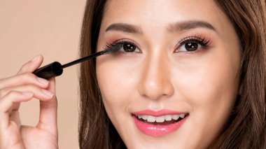 Closeup ardent young woman putting mascara on her long eyelashes with brush. Beauty cosmetic concept. Female model with perfect skin.