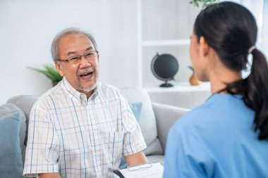 Caring young female doctor examining her contented senior patient with stethoscope in living room. Medical service for elderly, elderly sickness, declining health.