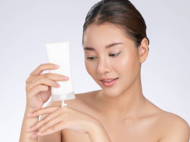 Gorgeous woman smiling holding mockup product for advertising text place, light grey background. Concept of healthcare for skin, beauty care product for advertising.