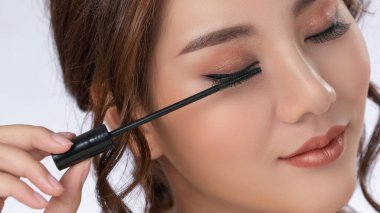 Closeup gorgeous young woman putting black mascara on her long eyelashes with brush. Beauty cosmetic concept. Female model with perfect skin.