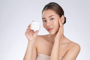 Gorgeous woman smiling holding mockup product for advertising text place, light grey background. Concept of healthcare for skin, beauty care product for advertising.