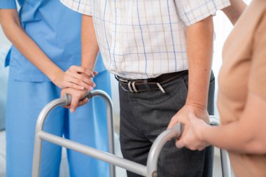 Contented senior man walking as he is helped by his wife and caretaker, walking with the aid of a folding walker. Nursing home for the elderly concept.