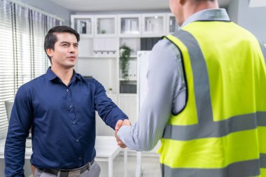 An engineer with a protective vest handshake with an investor in his office. Following a successful meeting, employee and employer form a partnership.