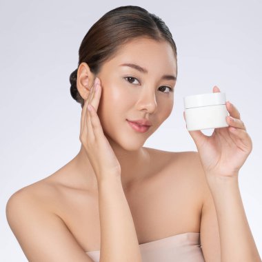Gorgeous woman smiling holding mockup product for advertising text place, light grey background. Concept of healthcare for skin, beauty care product for advertising.