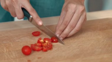 Close up hands holding a knife preparing a contented meal. Sliced tomatoes and other vegetables on the glass dish.