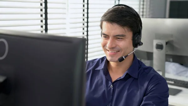 Young competent asian male call center agent working at his computer while simultaneously speaking with customers. Concept of an operator, customer service agent working in the office with headset.